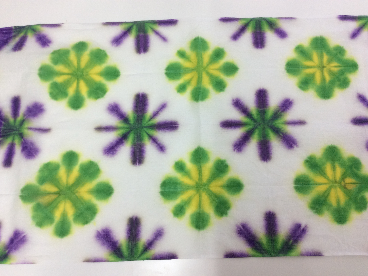 手ぬぐい 雪花絞りです。布を折りたたんで板で挟み輪ゴムで固定し、染め液に浸します。板をはずして、布を広げると雪の結晶のような模様があらわれます。