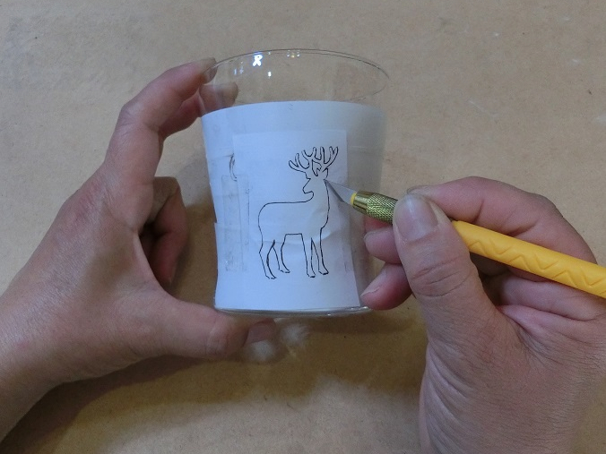 紙に描いておいたイラスト共にマスキングテープを貼り付けて、グラスをカバーします。 ラインに沿ってカッターで切り込みを入れてゆきます。