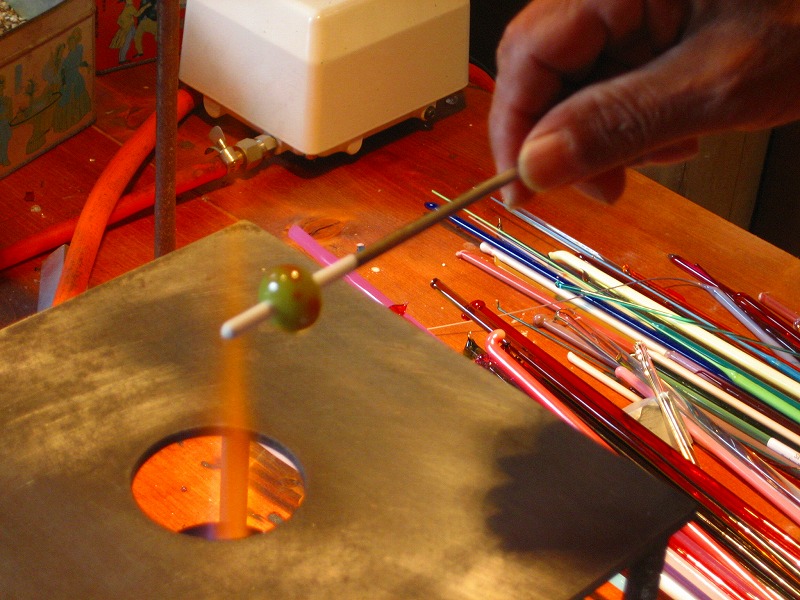 とんぼ玉をガスバーナーの炎の上がガラス棒を溶かしながら、ステンレス棒に巻き付けて制作します。