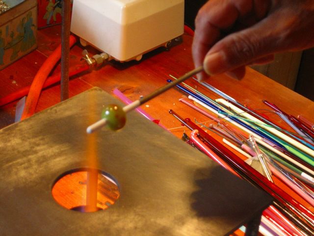 とんぼ玉をガスバーナーの炎の上がガラス棒を溶かしながら、ステンレス棒に巻き付けて制作します。