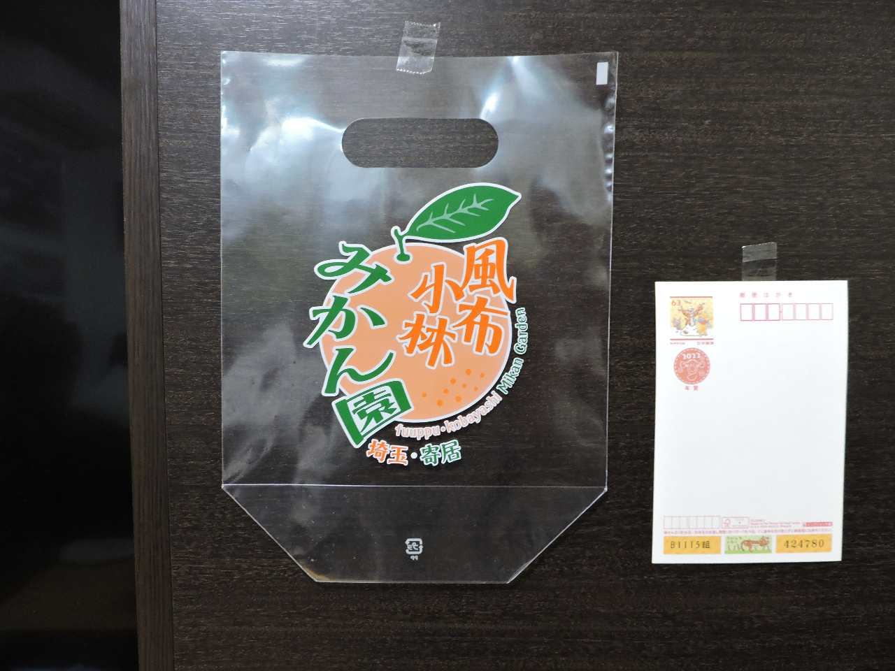 ご自身でもぎ取っていただくお土産袋(令和5年度新調しました)です。大きさが分かるようハガキと比較しました。約1.5kg入ります。