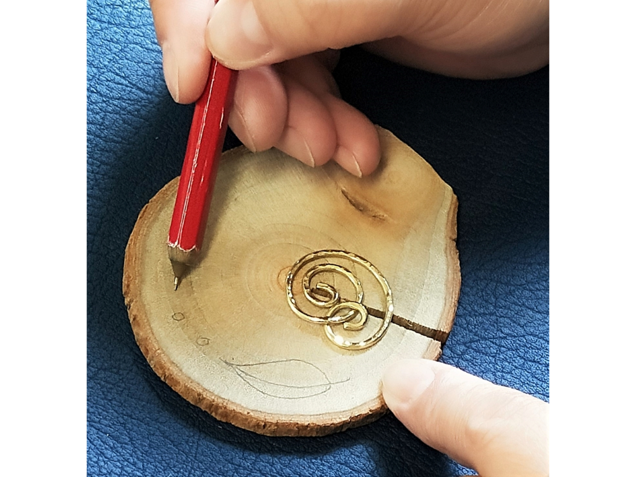 真鍮の渦巻きと丸板のバランスをみながら、絵や文字入れと穴あけの下書きをします。その後電気ペンで焦がしながら描いていきます。